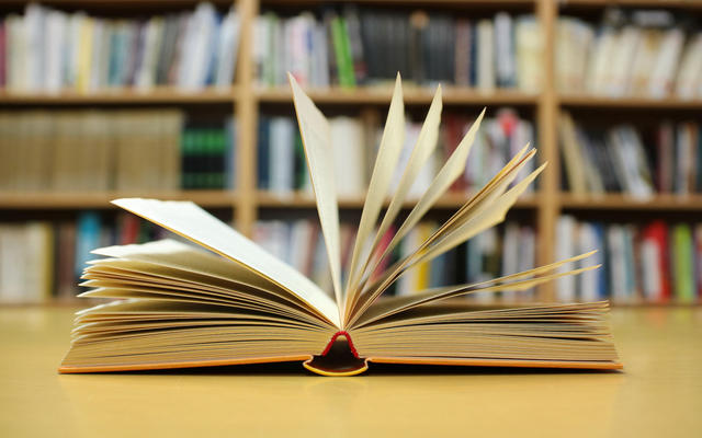 Photo of a book opened, against a backdrop of a bookshelf
