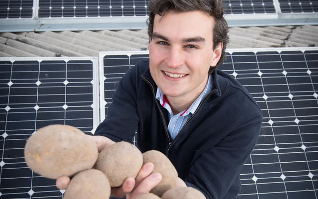 Josh Burton stood amongst solar panels, holding potatoes