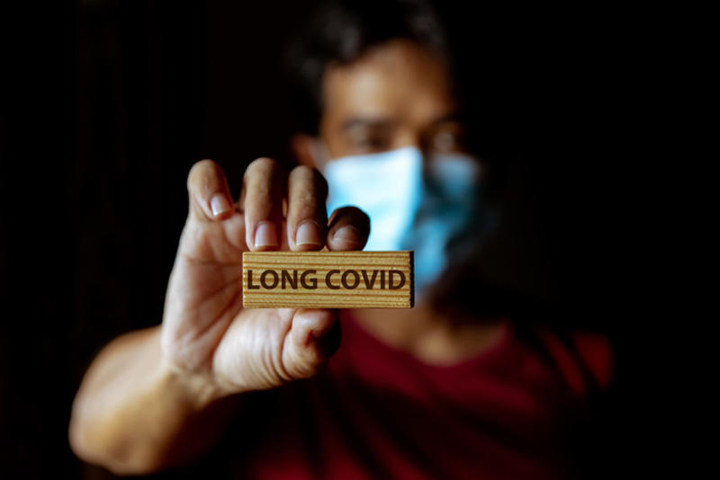 Masked man holds up piece of wood that says, 'Long Covid'