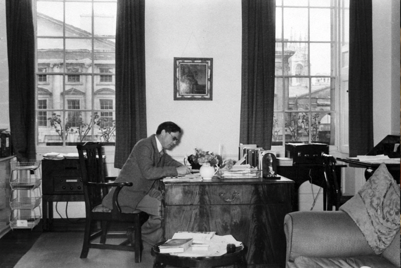 A blacl and white picture of Hugh Trevor Roper working at a desk, with part of Christ Church college visible through the window behind him