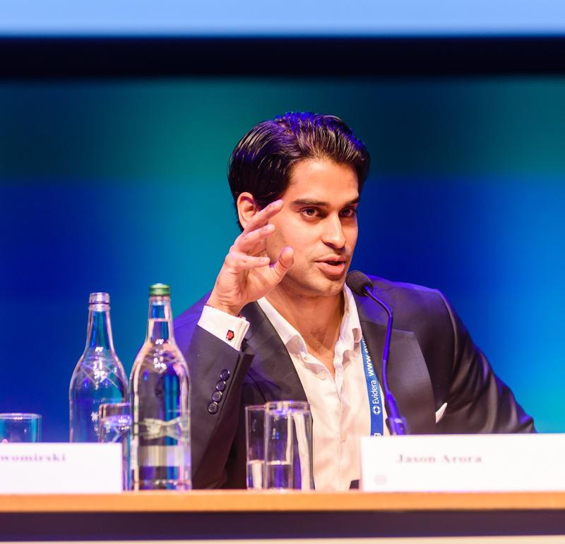 Jason Arora seated, speaking at a conference