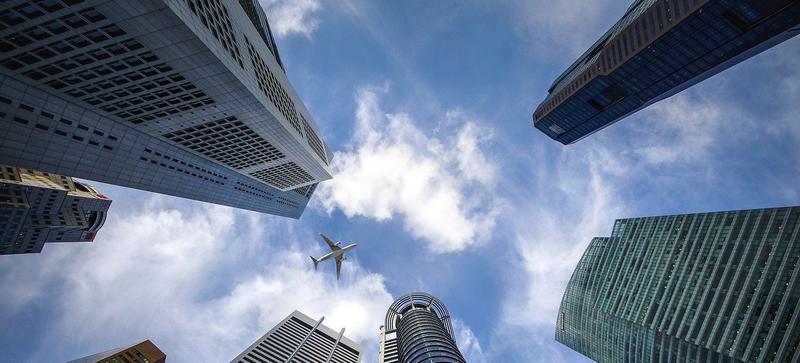 A view from groundlevel vertically upwards through skyscrapers, with an aeroplane flying above them